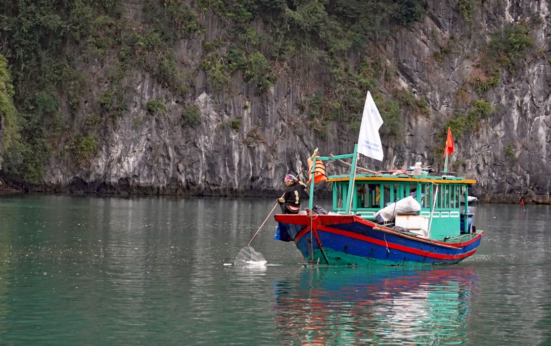 Fischerboot, das Müll in der Halong Bucht sammelt